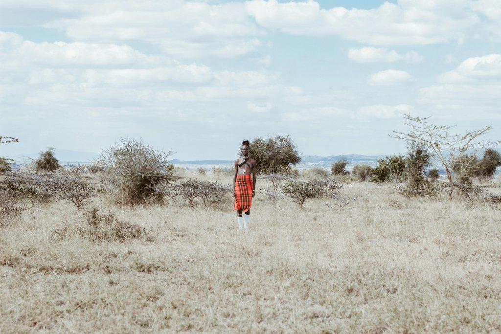 pexels-photo-2600207-2600207 A person in traditional Kenyan attire stands in a vast grass field under a cloudy sky.
